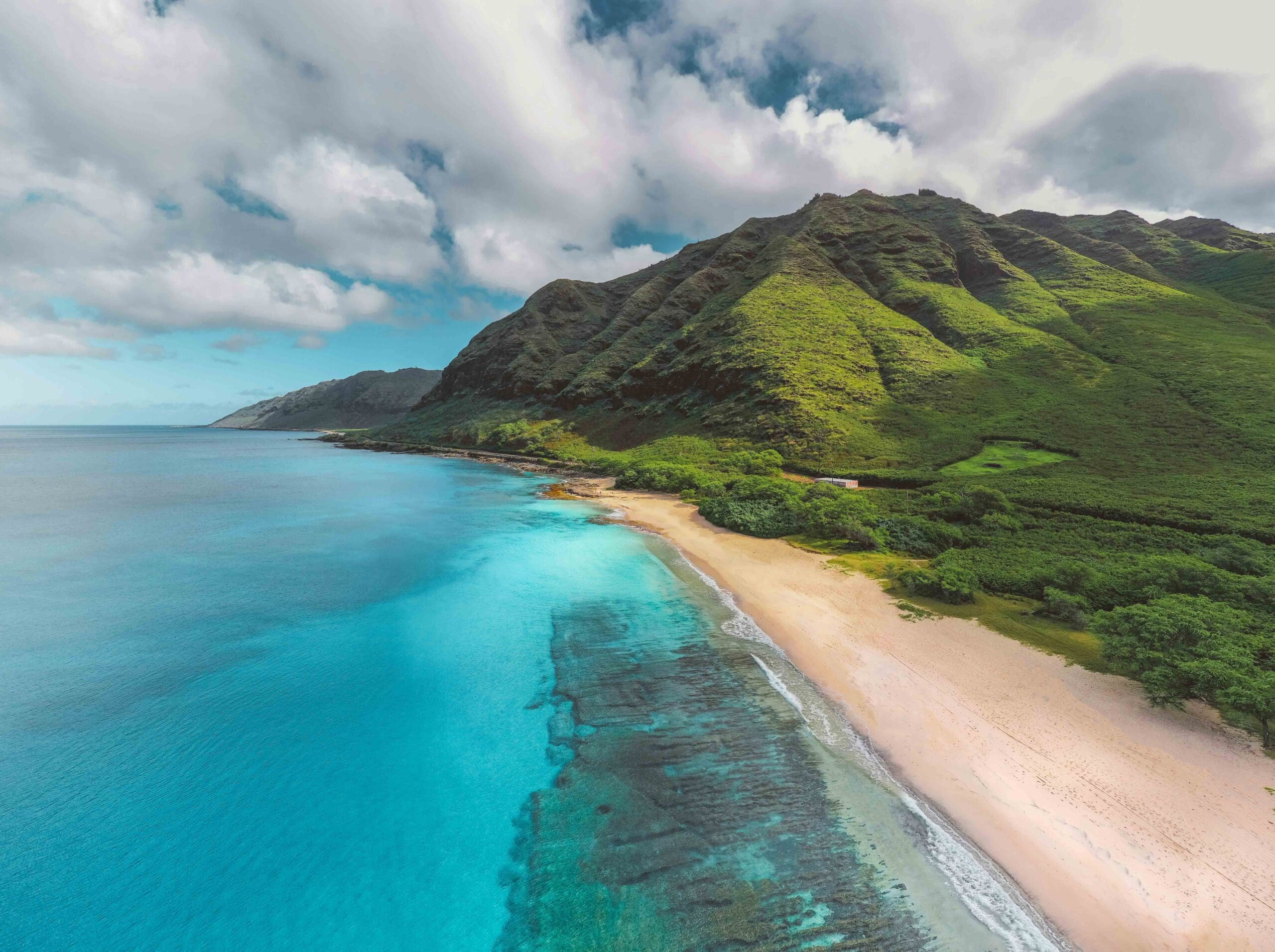 Coast of Hawaii featuring blue and clear water, sandy shores, and tall green mountains